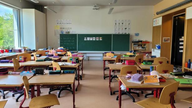 Klassenzimmer mit mehreren Tischen und einer grünen Tafel