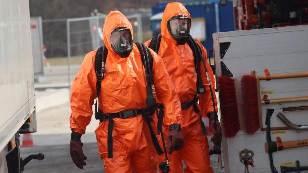 Zwei Personen in orangen Schutzanzügen mit Schutzmasken