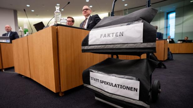Ein Rollwagen mit den Aufschriften „FAKTEN“ und „STATT SPEKULATIONEN“ steht in einem Konferenzraum mit mehreren Personen.