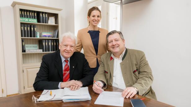 Eine Frau steht hinter zwei sitzenden Männern.