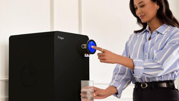 Eine Frau füllt ein Wasserglas an einem Wasserspender auf.