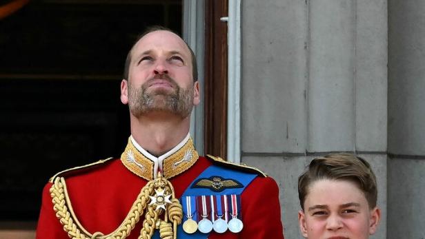 Prinz William steht mit seinen Söhnen George und Louis auf einem Balkon und schaut nach oben.