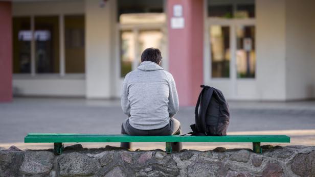 One young man sitting on bench at school yard. Break time. Back view.
