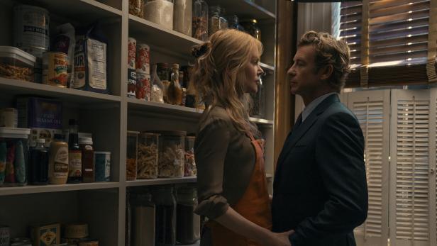 Eine Frau mit Schürze und ein Mann im Anzug stehen sich in einer Vorratskammer gegenüber und halten sich an den Händen.