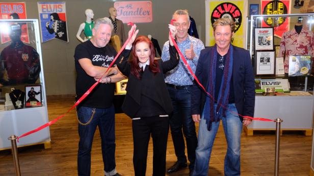 Priscilla Presley und andere durchschneiden ein rotes Band bei einer Veranstaltung.