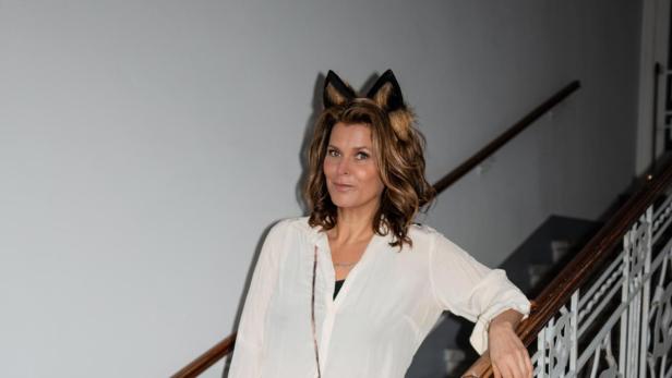 Janina Lebiszczak steht mit Katzenohren, einer Katzentasche und buntem Schal auf einer Treppe, passend zu ihrem Buch über Wiens Katzen.