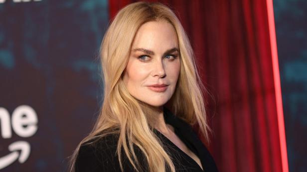 Nicole Kidman mit blonden Haaren und dunklem Blazer vor einem roten Vorhang.
