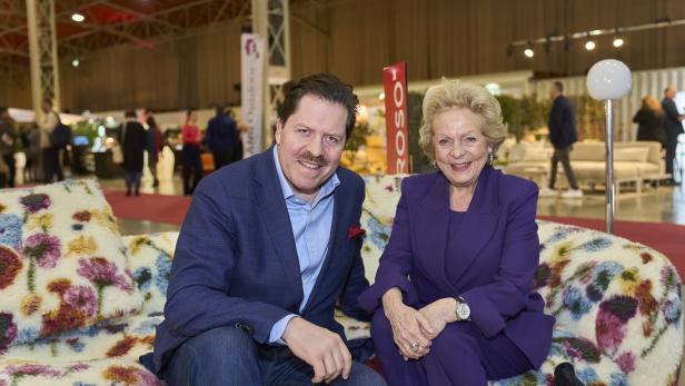 Zwei Personen sitzen auf einem Sofa mit Blumenmuster in einer Halle.