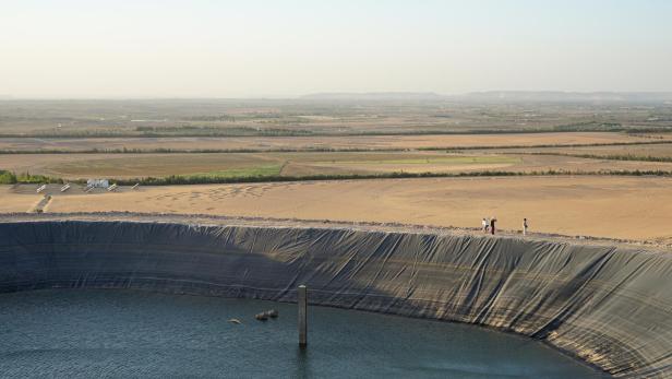 Großer künstlicher Wasserspeicher am Rand einer Wüstenlandschaft mit mehreren Personen am Beckenrand.
