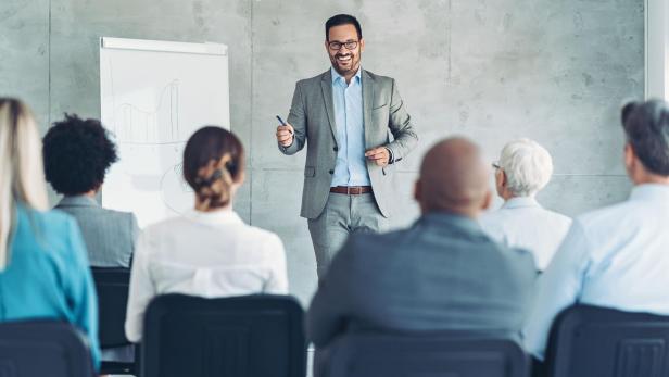 Ein Mann im Anzug bei einer Präsentation in einem Geschäfts-Meeting steht neben einem Flipchart