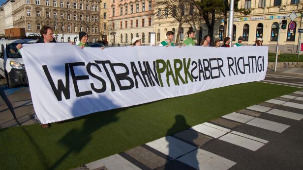 Mehrere Menschen halten ein langes Transparent mit der Aufschrift „WESTBAHNPARK? ABER RICHTIG!“ auf einer Straße.