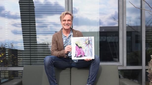 Ein Mann sitzt auf einem Sofa und hält ein Bild mit einer farbenfrohen Illustration.