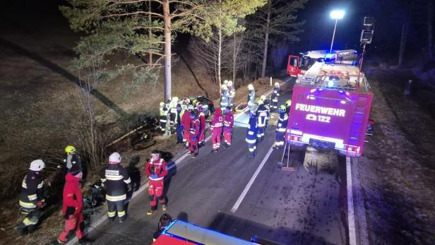 Ein Foto von dem Feuerwehreinsatz von oben. Mehrere Personen und Feuerwehrautos stehen nachts auf dem Straße neben dem Unfallfahrzeug.