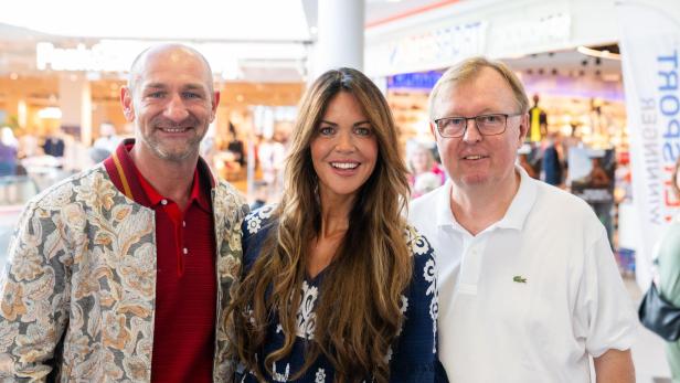 Drei Personen lächeln gemeinsam in einem Einkaufszentrum in die Kamera.