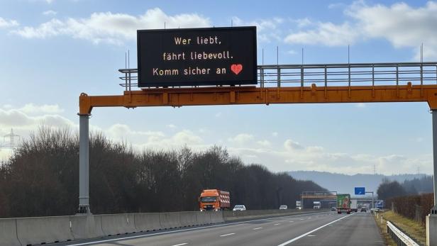 Ein Foto von der Autobahn und einer Anzeige darüber, auf der "Wer liebt, fährt liebevoll. Komm sicher an" steht.
