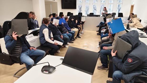 Angeklage halten sich Aktenordner vors Gesicht.