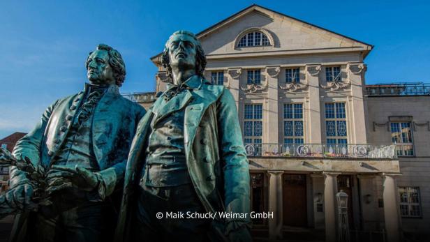 Goethe- und Schiller-Denkmal vor dem Deutschen Nationaltheater in Weimar bei blauem Himmel.