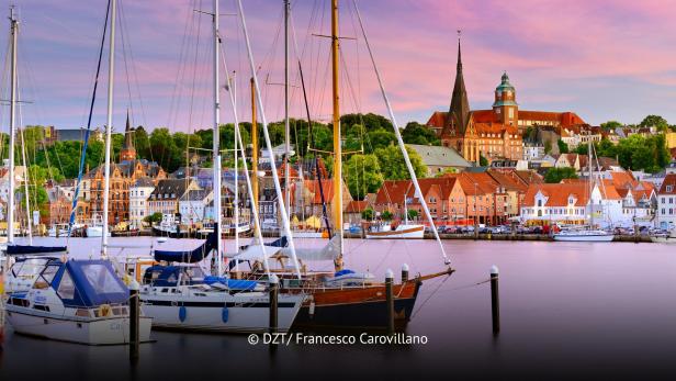 Segelboote im Hafen vor historischer Altstadtkulisse und Kirchen bei Sonnenuntergang in Flensburg.