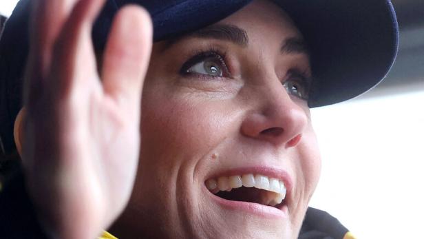 Prinzessin Kate lächelt, trägt eine blaue Kappe und eine gelbe Jacke und winkt.