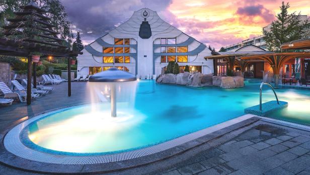 Ein Pool mit einem Brunnen und Wasserfeatures bei Sonnenuntergang, der eine ruhige und entspannende Atmosphäre schafft.