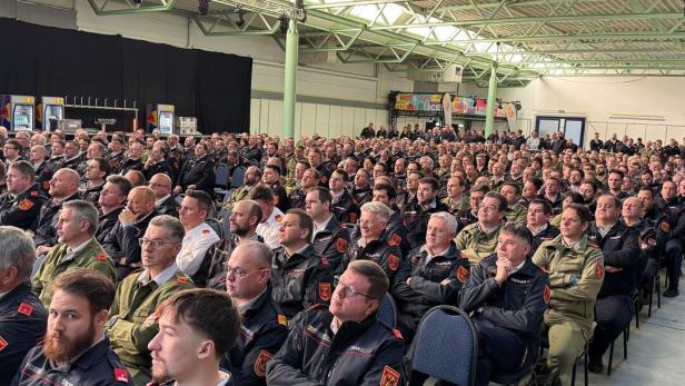Viele Feuerwehrleute in Uniform sitzen dicht gedrängt in einer großen Halle und hören aufmerksam zu.