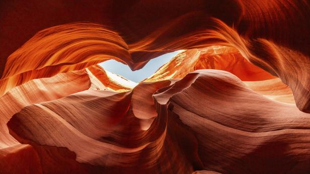 Rote, geschwungene Sandsteinformationen mit einem schmalen Blick auf den blauen Himmel in der Mitte.