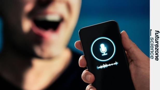 Eine Person spricht vor ein Smartphone, auf dessen Display ein leuchtendes Mikrofon-Symbol und eine Tonspur zu sehen sind.