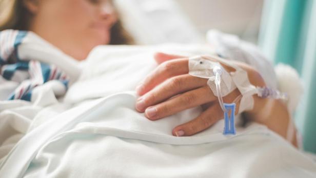 Hand einer Patientin mit Infusionsnadel auf einer Krankenhausdecke.
