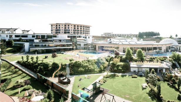 Große Hotelanlage mit mehreren Gebäuden, Außenpool, Spielplatz und weitläufigen Grünflächen bei sonnigem Wetter.