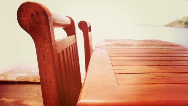 Holztisch und zwei Holzstühle mit Blick auf einen hellen, unscharfen Hintergrund.