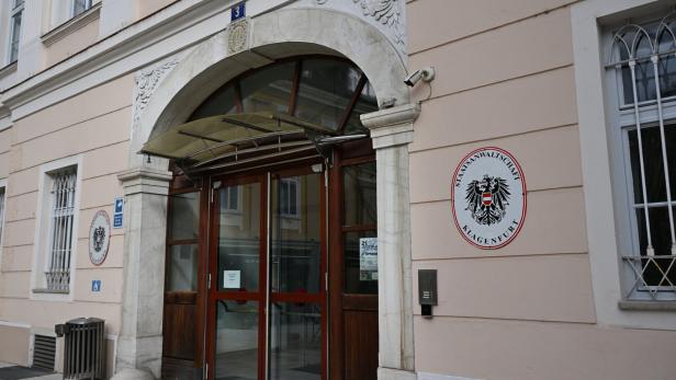 Eingang eines Amtsgebäudes mit dem Wappen der Staatsanwaltschaft Klagenfurt an der Wand.