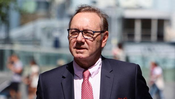 Kevin Spacey mit Brille, Anzug und roter Krawatte blickt in die Ferne.