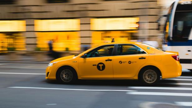 Gelbes New Yorker Taxi fährt schnell an einer Straße mit unscharfem Hintergrund vorbei.