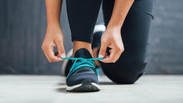 Eine Person kniet und bindet ihre türkisfarbenen Schnürsenkel an einem dunklen Turnschuh.
