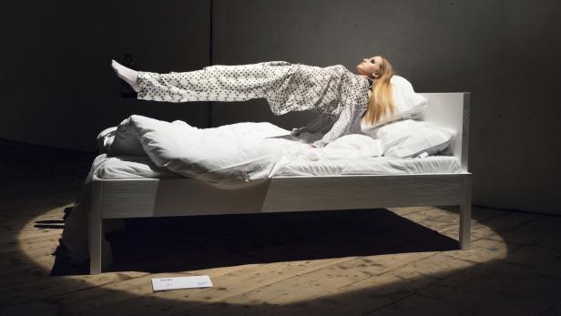 Eine Frau in Pyjamas schwebt über einem weißen Bett.