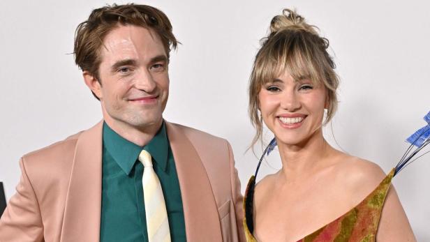 Robert Pattinson im rosa Anzug mit grünem Hemd, Suki Waterhouse in einem bunten Kleid.