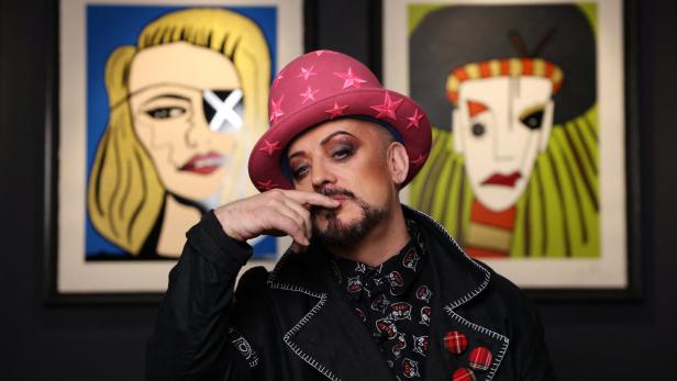 Boy George posiert mit Sternen-Hut vor zwei gerahmten Kunstwerken.