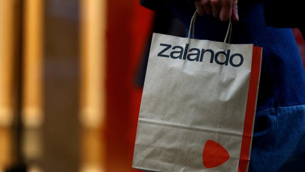 Eine Hand hält eine braune Papiertüte mit dem Zalando-Logo und einem orangefarbenen Dreieck.