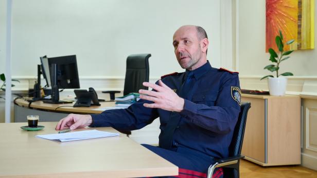 Ein Polizist in Uniform sitzt an einem Schreibtisch und gestikuliert während eines Gesprächs.