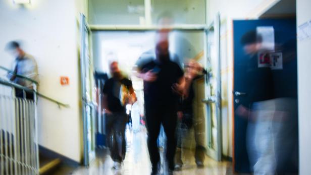 Mehrere unscharfe Personen bewegen sich durch einen Flur einer Schule während einer Pause.