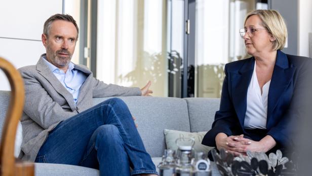 Zwei Personen sitzen auf einem Sofa und führen ein Gespräch in einem modernen Büro mit Glaswänden.