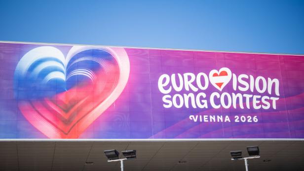 Großes Plakat mit Herzmotiv und Schriftzug „Eurovision Song Contest Vienna 2026“ vor blauem Himmel.