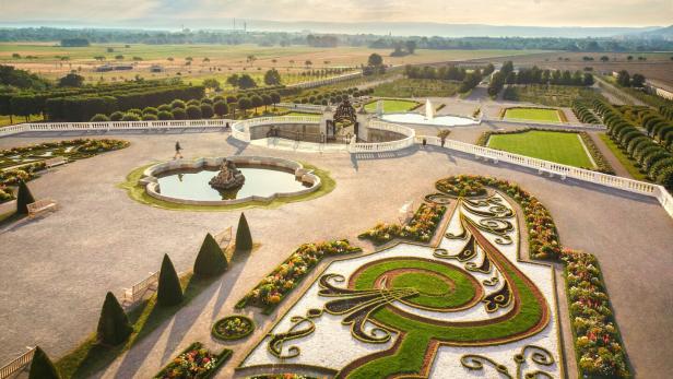 Die weitläufige Gartenanlage von Schloss Hof besticht durch kunstvolle Blumenbeete, gepflegte Wege und mehrere Brunnen vor einer ländlichen Kulisse.