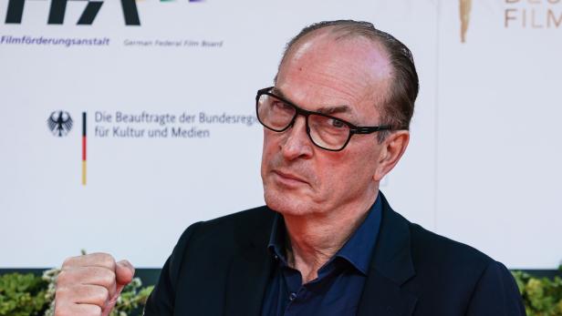 Ein Mann mit Brille und ernstem Gesichtsausdruck hebt die Faust, trägt dunkles Sakko und Hemd.