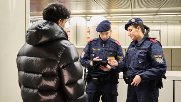 Zwei Polizistinnen kontrollieren die Ausweisdokumente eines Mannes in einer Bahnhofshalle.