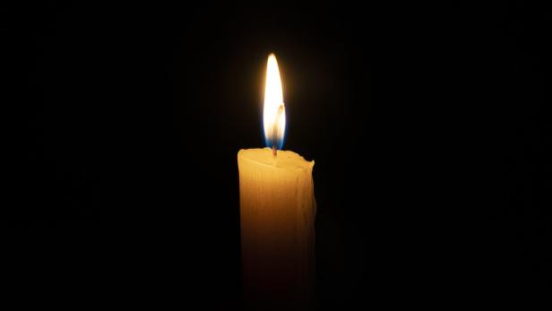 orange candle burns in the dark on a black background. The concept of memory and sorrow.