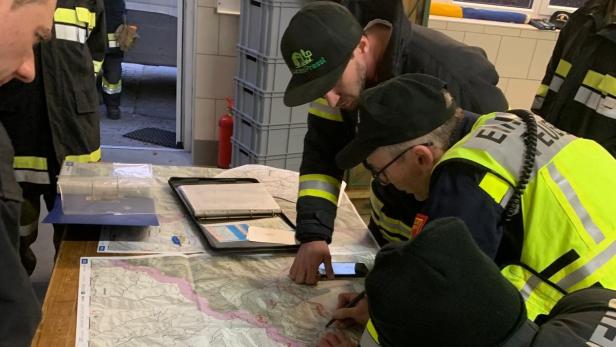 Einsatzkräfte der Feuerwehren Rohr im Gebirge und Gutenstein besprechen an einer großen Karte das Suchgebiet für die vermisste Person.