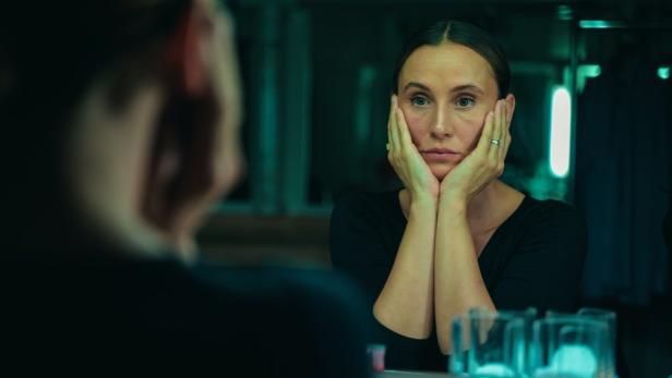 Peri Baumeister spielt Wissenschaftlerin Elena und blickt mit beiden Händen an den Wangen in einen Spiegel