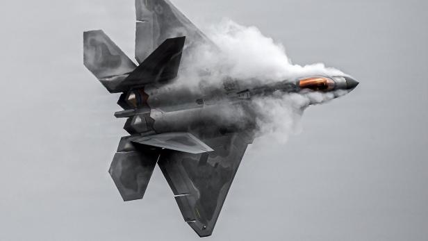 Ein Kampfjet des Typs F-22 Raptor fliegt vor grauem Himmel