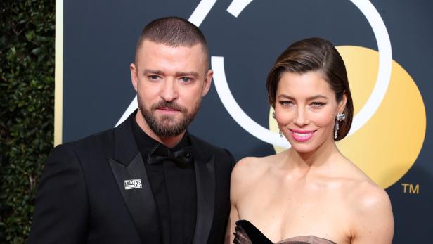 Justin Timberlake und Jessica Biel posieren auf einem Event vor goldenem Hintergrund.